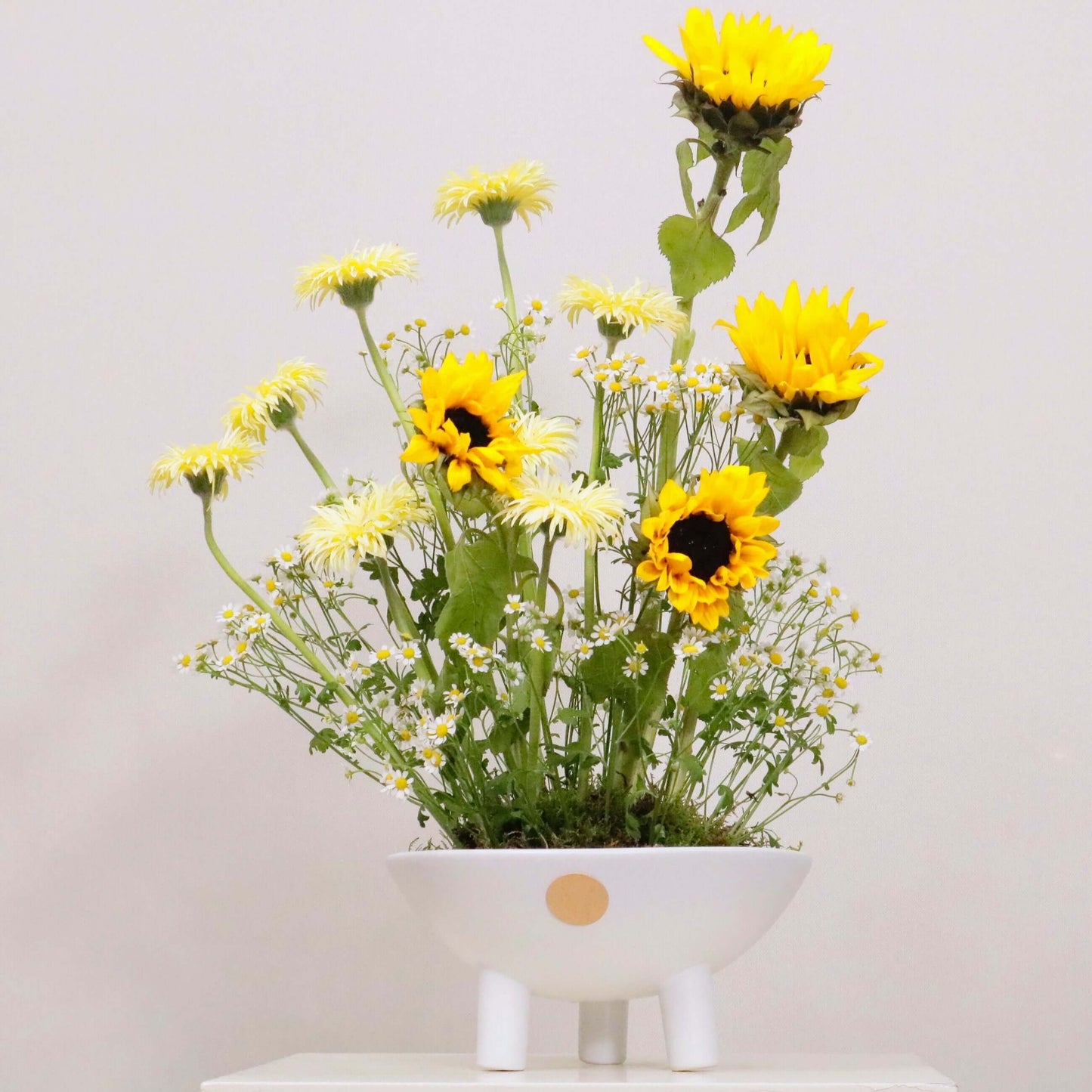 Aestas floral arrangement with sunflowers, yellow gerbera daisies, and matricaria in a white vase, bringing summer warmth and brightness.