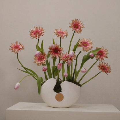 The perfect artistic luxury gift featuring pink gerberas and pastel tulips in a white ceramic vase.