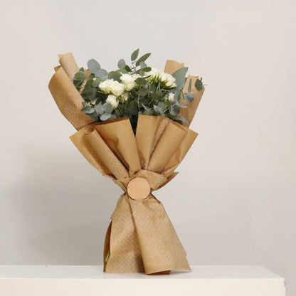 Hand-wrapped designer floral bouquets featuring premium white spray roses and eucalyptus in elegant packaging.
