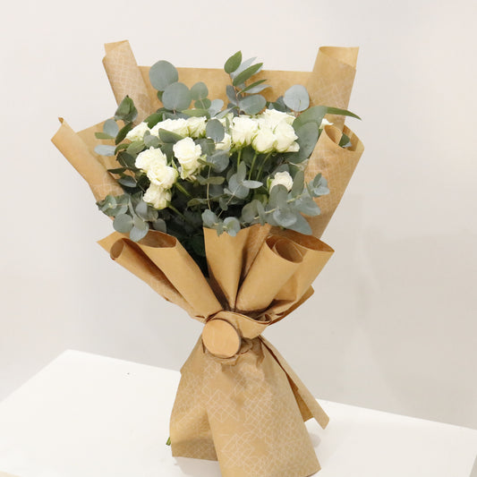 Hand-wrapped designer floral bouquets featuring white spray roses and eucalyptus in elegant wrapping.