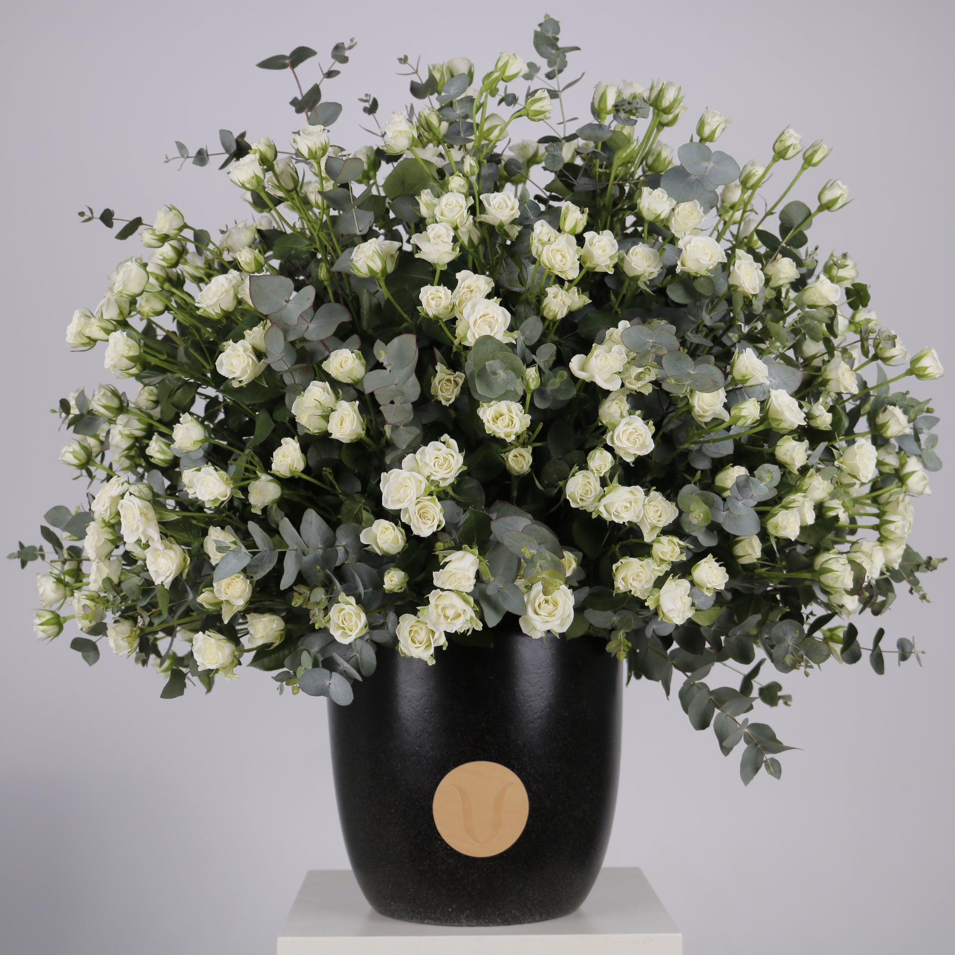 Premium arrangement of white spray roses and eucalyptus in a black pot, showcasing elegant floral design.