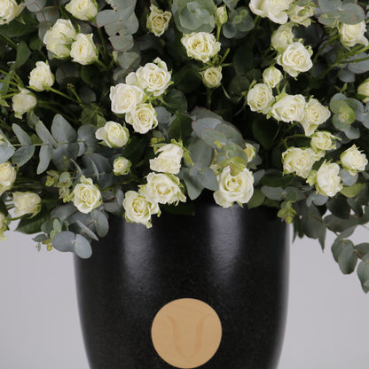 premium arrangement of white spray roses and eucalyptus in a stylish black pot with a wooden label.