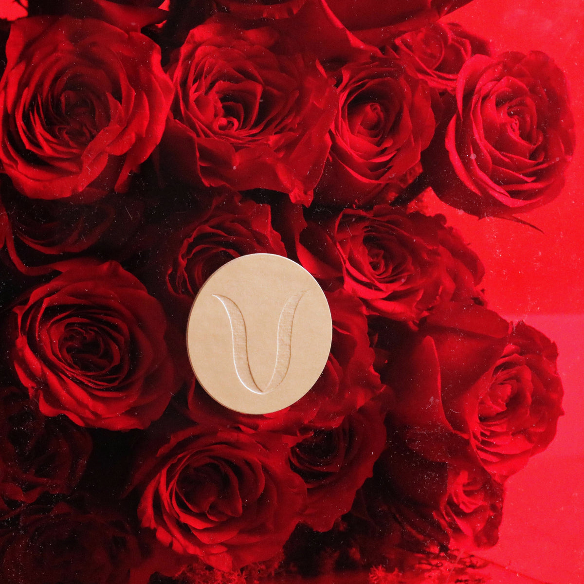Lush red roses elegantly arranged in a box with a decorative emblem, showcasing a romantic and luxurious floral design.