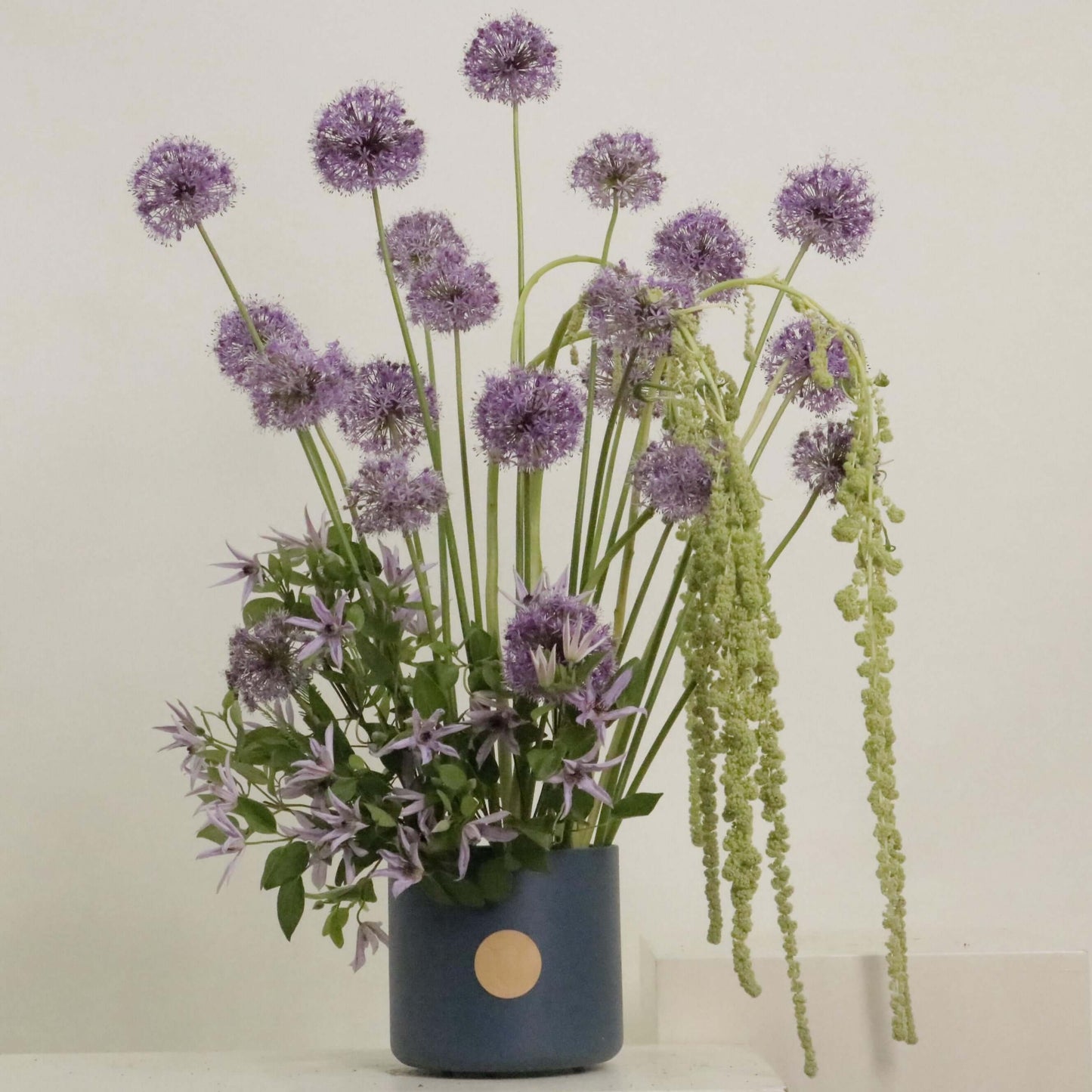 Elegant floral arrangement featuring Allium, clematis, and Amaranthus in a stylish blue vase.