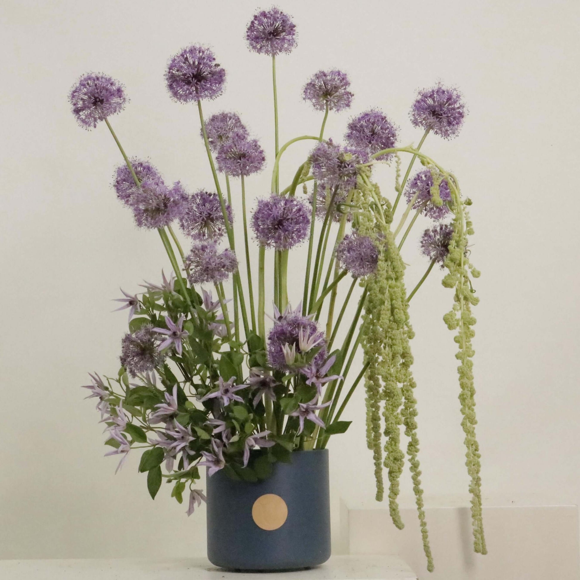 Elegant floral arrangement featuring Allium, clematis, and Amaranthus in a stylish blue vase.