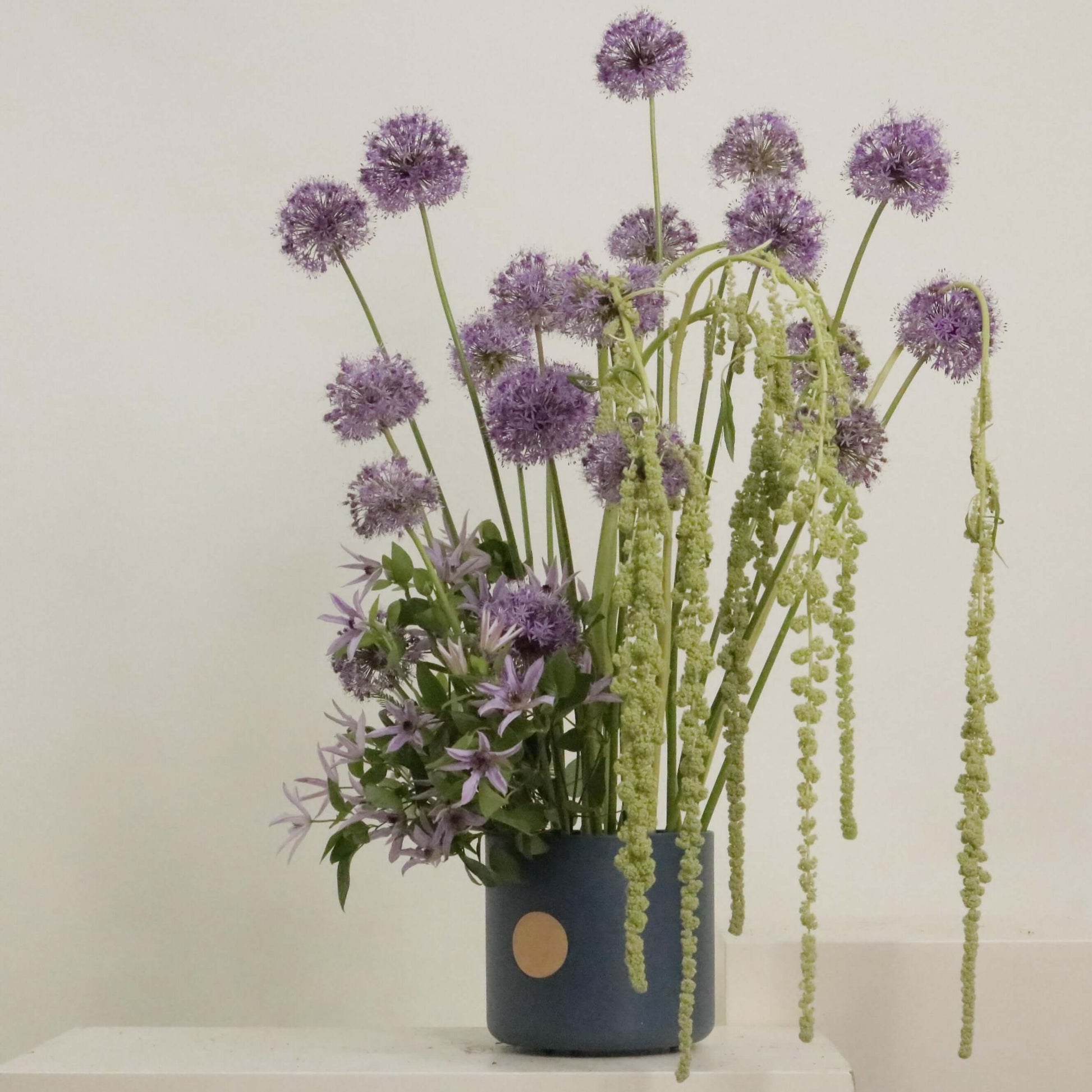 Elegant flower arrangement with Allium and clematis in blue vase, showcasing joyful purple and green hues.