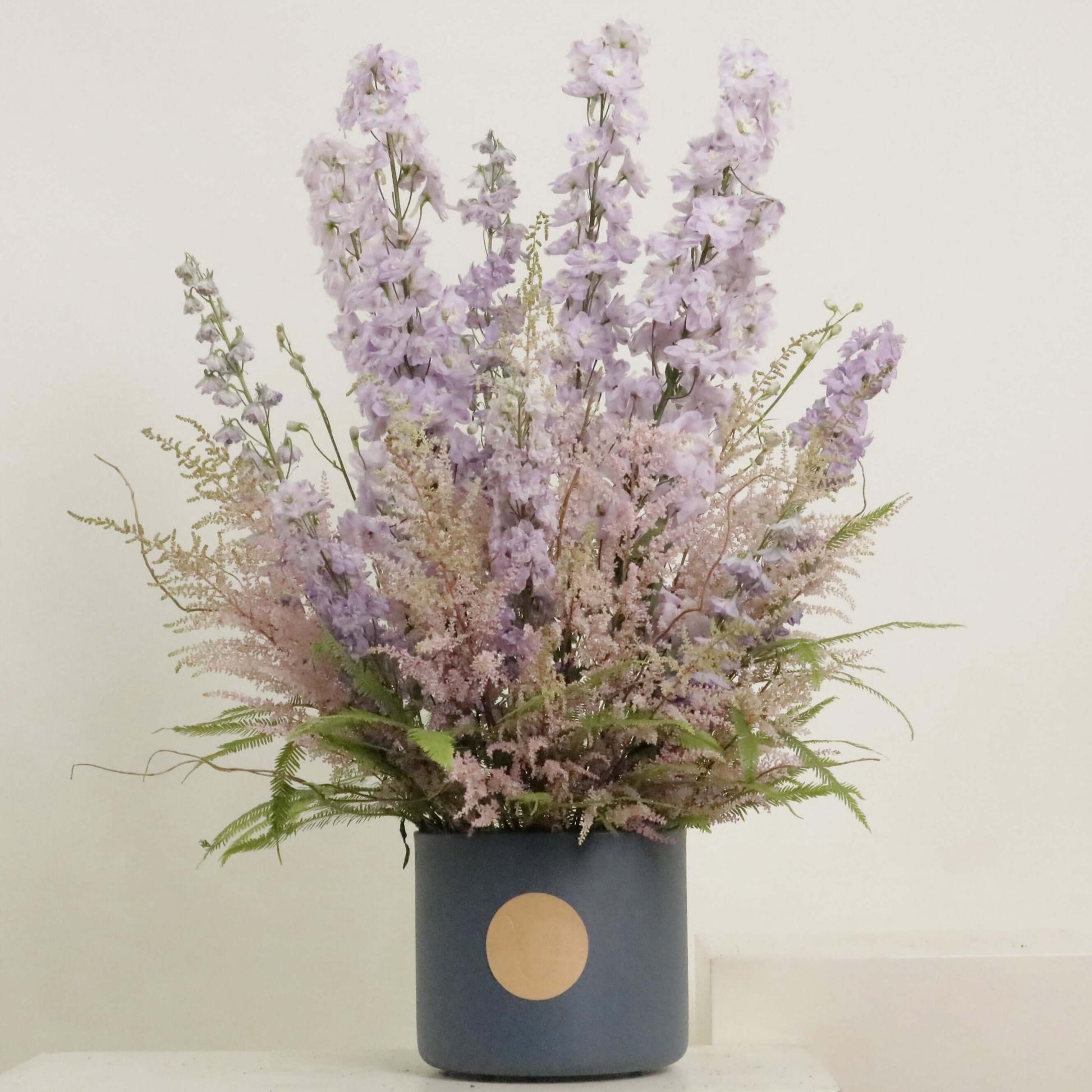 Elegant floral arrangement featuring Delphinium and Skimmia in a blue pot, capturing the joy of memories with blooms.