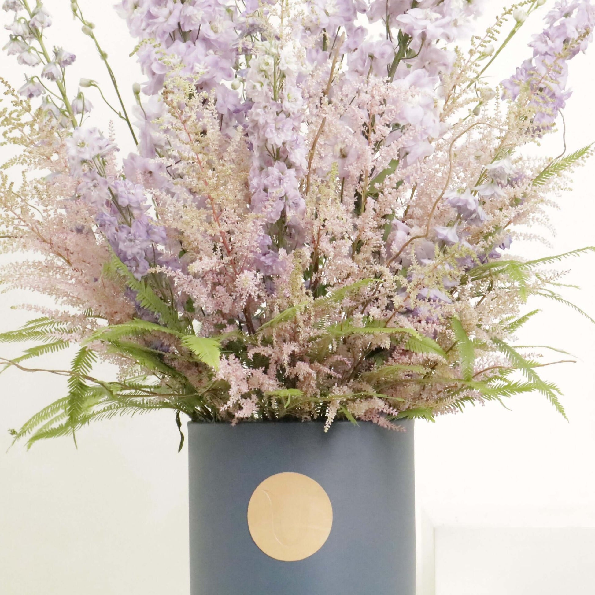 Elegant floral arrangement of Delphinium and Skimmia in a chic container, showcasing joyful hues of lavender and green.