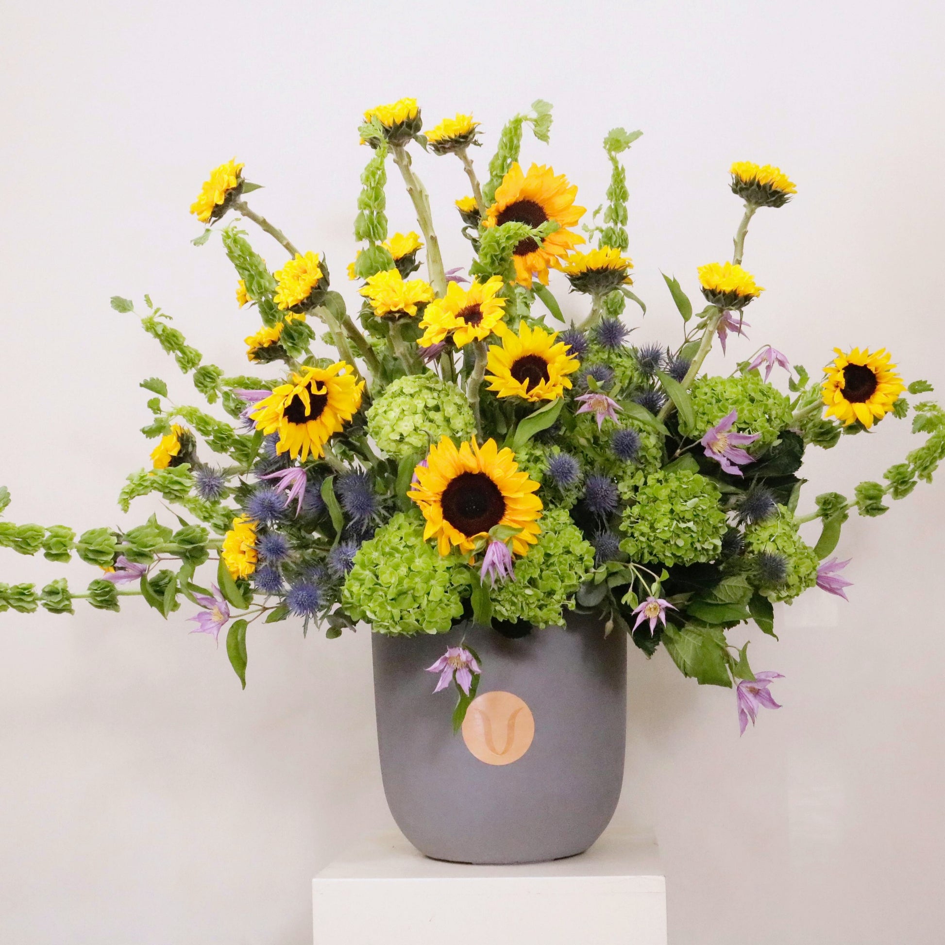 Luxurious floral arrangement with sunflowers, emerald green hydrangeas, and clematis in a stylish vase