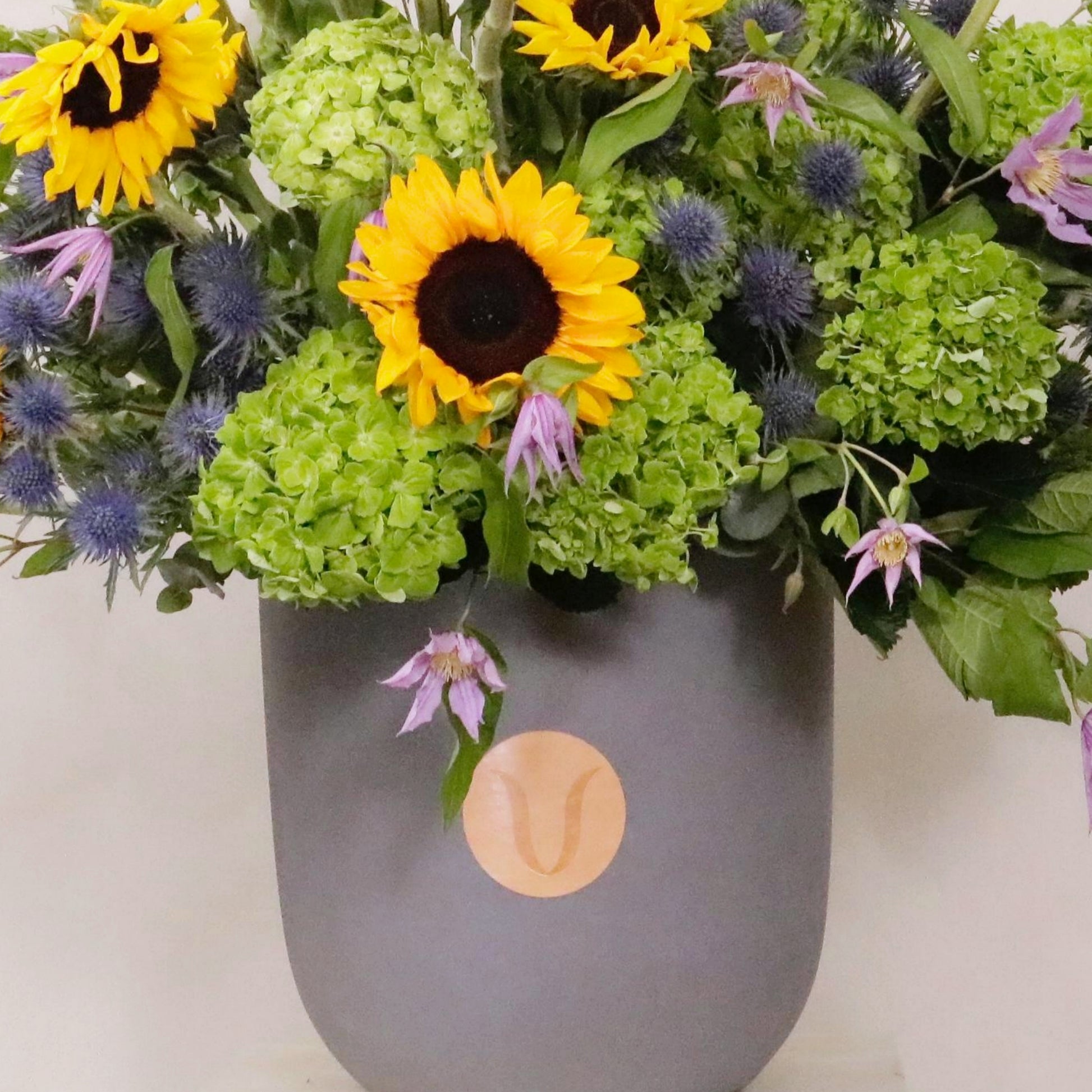 Luxurious Ver Royal floral arrangement with sunflowers, emerald hydrangeas, clematis, in a sleek vase. Celebrates spring freshness.