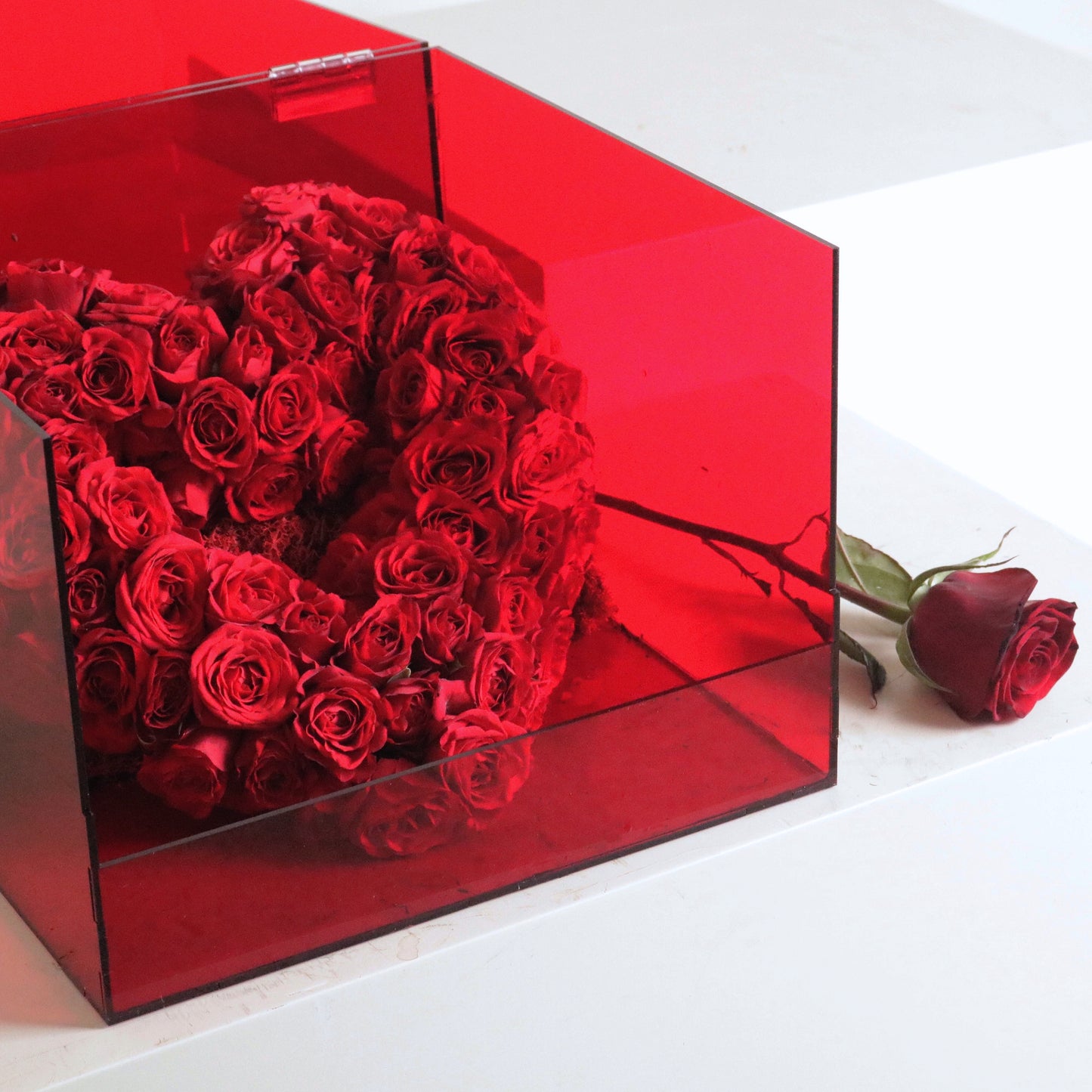 Luxurious heart-shaped arrangement of vibrant red spray roses in a transparent box, symbolizing love and passion.
