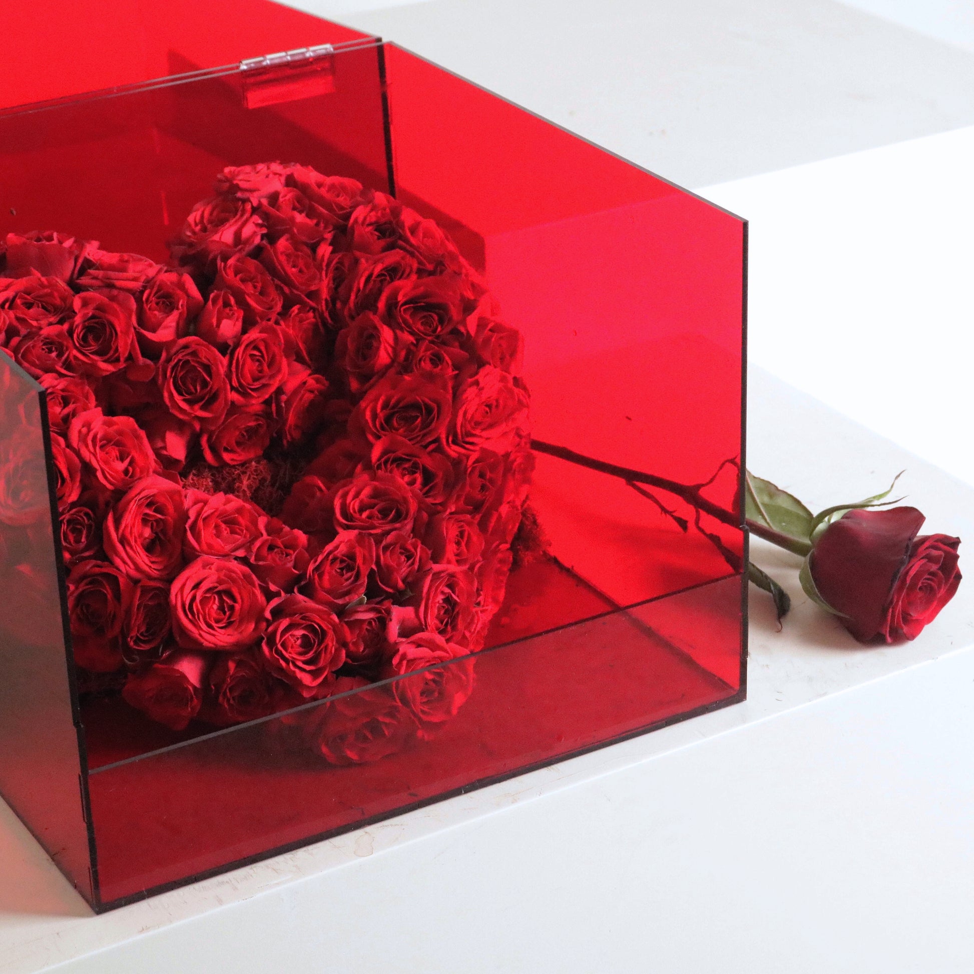 Luxurious heart-shaped arrangement of vibrant red spray roses in a transparent box, symbolizing love and passion.