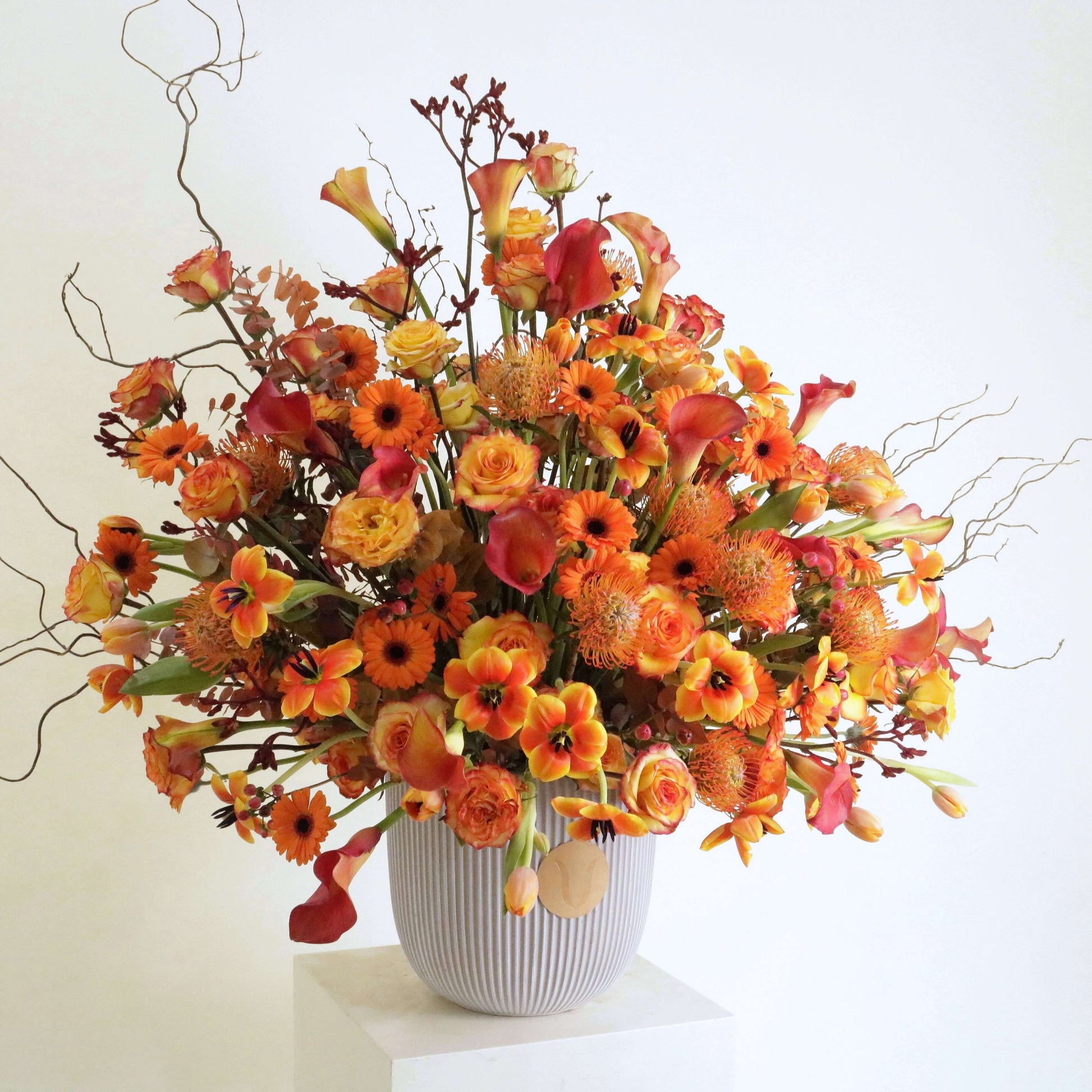 Elegant floral arrangement featuring orange calla lilies and rosa corolla branches inspired by a Kuwaiti sunset, Sunset Symphony design.