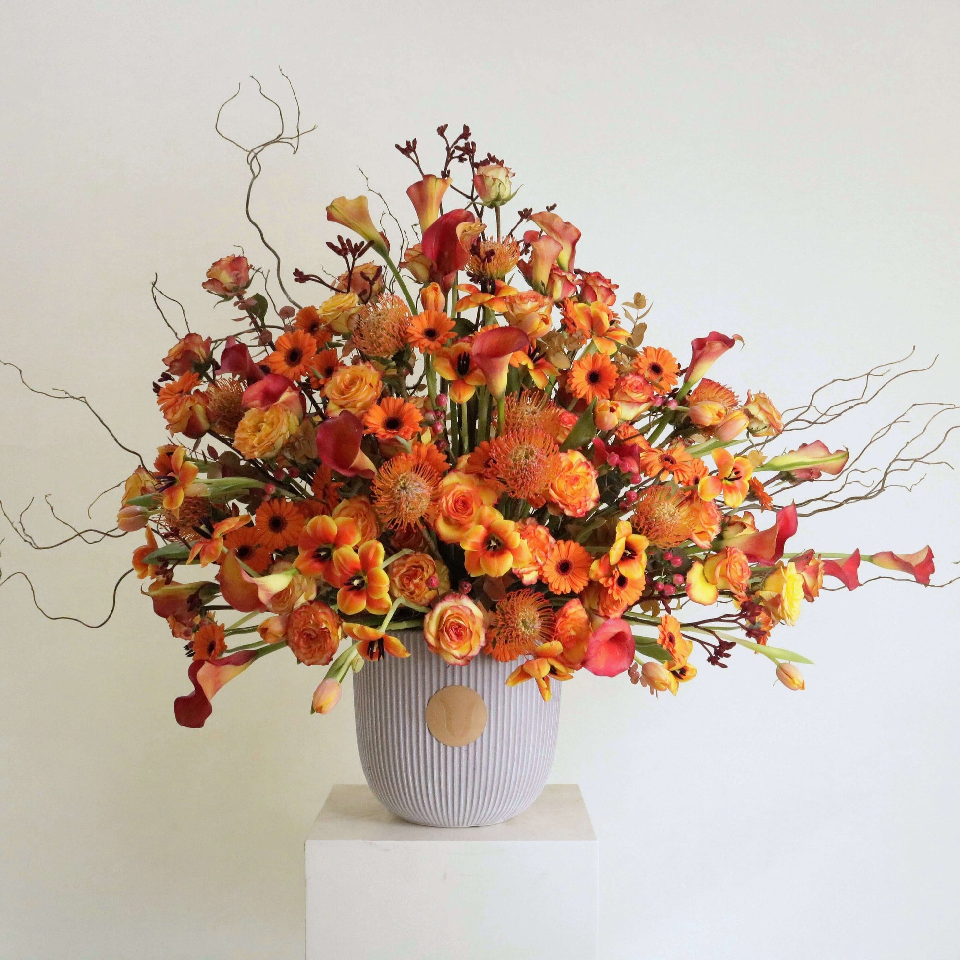 Sunset Symphony floral arrangement with orange calla lilies, rosa corolla branches, inspired by Kuwaiti sunset, expressing warmth and elegance.